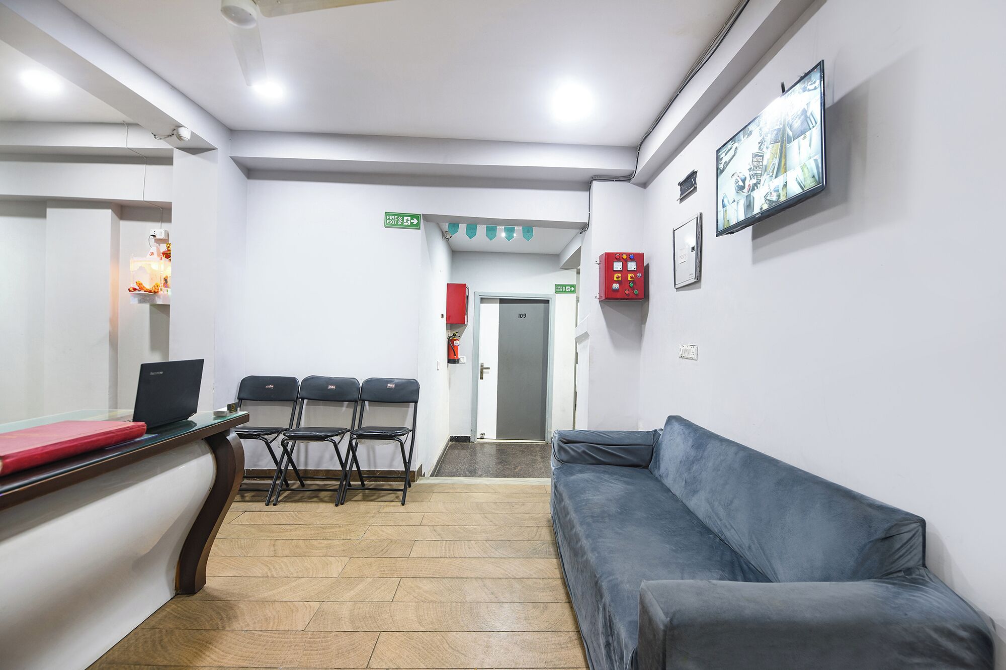 Un espace d’accueil comprenant un comptoir, des chaises, un canapé, un panneau indiquant la sortie de secours et un boîtier d’alarme incendie.