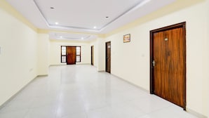 A hallway with white tiled flooring, wooden doors, and recessed ceiling lighting. - Fabhotel Vsm Suites (Hyderabad)
