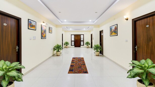 A hotel corridor with wooden doors, potted plants, and framed artwork on the walls. - Fabhotel Vsm Suites (Hyderabad)