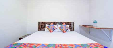 A bed with a colorful geometric-patterned bedspread, two pillows with a similar design, a wooden headboard, and a small table with a water bottle beside the bed.