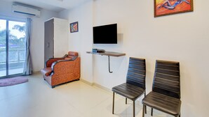 Ein modernes Zimmer mit einer Couch, zwei schwarzen Sesseln, einem Flachbildfernseher und Kunstwerken an den Wänden.