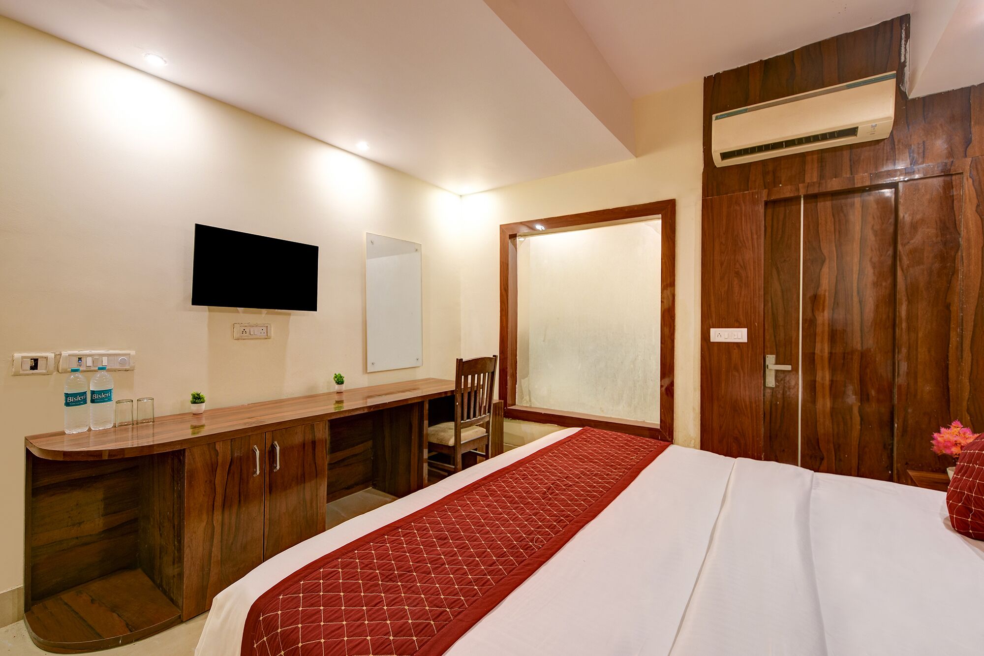 Habitación de hotel con cama, escritorio de madera, televisor montado en la pared y aire acondicionado.