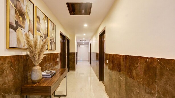 A hallway with a marble floor, a wooden console table with a vase and books, and framed artwork on the walls. - Fabhotel Golden Key Residency (New Delhi)