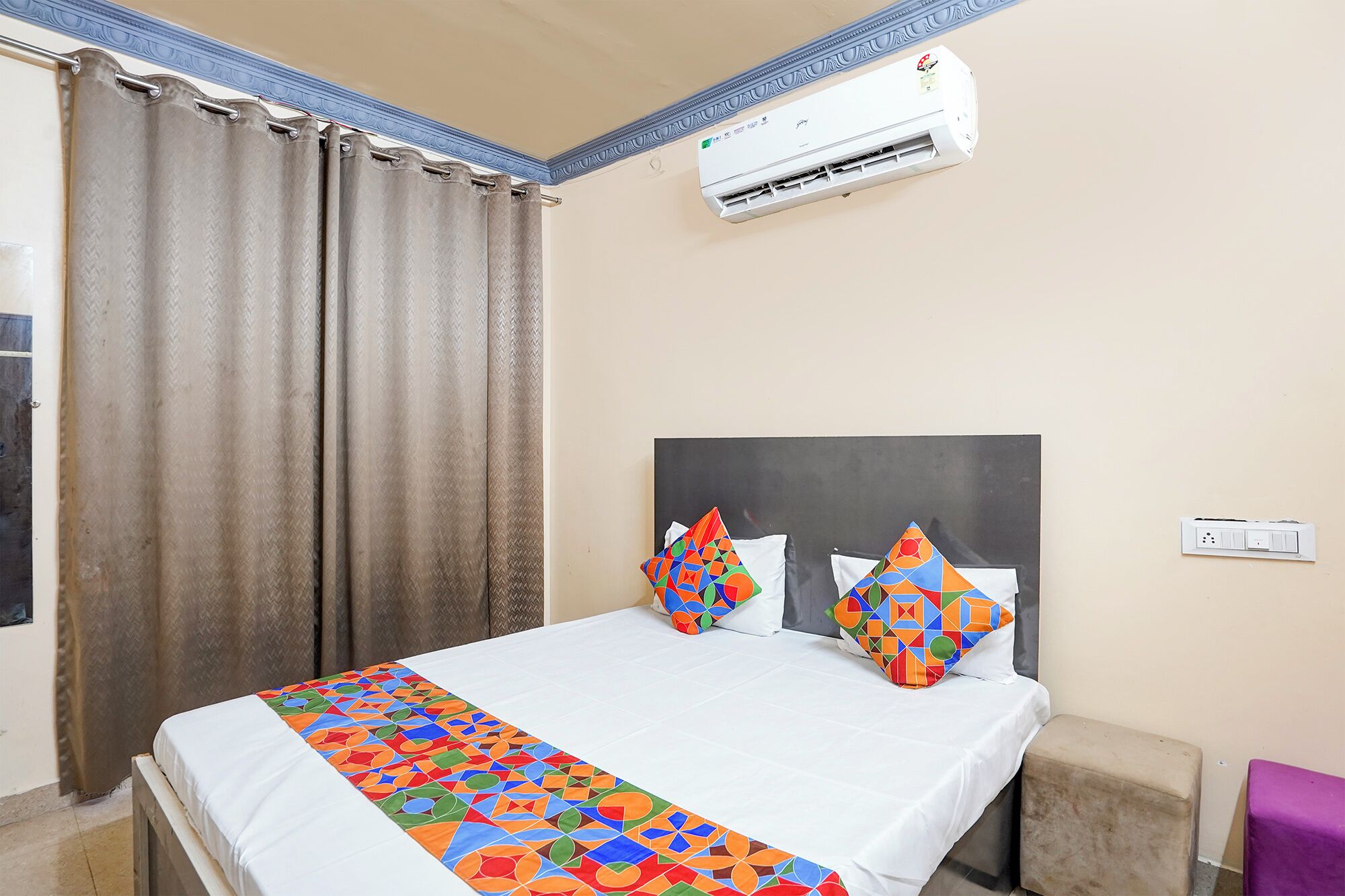 A hotel room with a bed, curtains, an air conditioner, and a colorful bedspread.