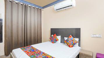 A hotel room with a bed, curtains, an air conditioner, and a colorful bedspread.
