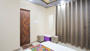 A room with a wooden door, a white wall, a mirror, a bed, a colorful rug, and a curtain. - Fabhotel Imperial Blue (Nagpur)