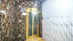 A narrow hallway with a textured wall and a wooden floor leading to a door with a 'LIFT' sign. - Via Red Apple Greater Kailash (New Delhi)