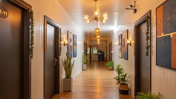 A hotel hallway with wooden floors, dark doors, and framed artwork on the walls. - Via Red Apple Greater Kailash (New Delhi)