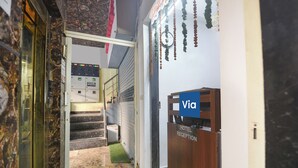 A reception area with a reception desk, a clock, and a staircase leading to an elevator. - Via Red Apple Greater Kailash (New Delhi)