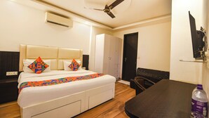 A hotel room with a bed, a desk, a wardrobe, a ceiling fan, and an air conditioning unit. - Via Red Apple Greater Kailash (New Delhi)