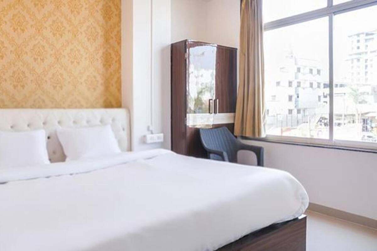 Une chambre d’hôtel avec un lit, une chaise, une armoire et une fenêtre donnant sur la ville.