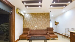 A modern waiting area with a brown sofa, a coffee table, and a small dining table with chairs. - Fabhotel Golden Palm (New Delhi)