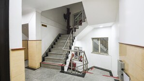 A staircase with a metal handrail, a fire extinguisher, and a small window on the wall. - Fabhotel Golden Palm (New Delhi)