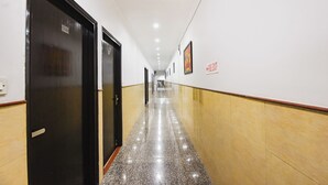A hallway with doors on the left, a fire exit sign on the right, and a polished floor. - Fabhotel Golden Palm (New Delhi)