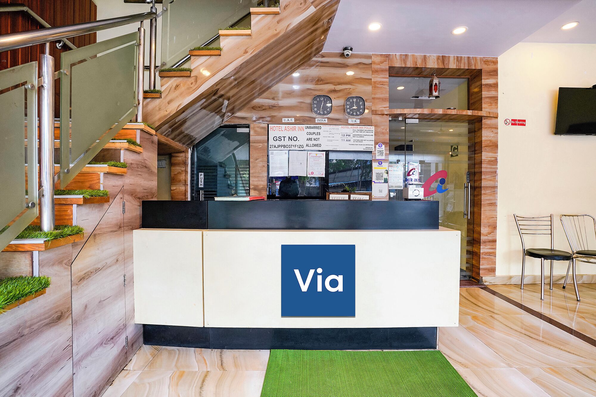 A reception desk with a 'Via' sign, a staircase with wooden steps and metal railings, and a 'No Smoking' sign on the wall.