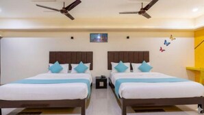 A hotel room with two beds, each with a wooden headboard and white bedding. There are ceiling fans above the beds, and a small nightstand between them. - Fabhotel D Grand (Madurai)