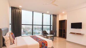 A hotel room with a large bed, a desk, two chairs, a TV, and a wardrobe. - Fabhotel Lotus Inn Pimpri Chinchwad (Pune)