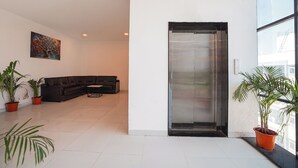 A modern lobby with a dark-colored sofa, potted plants, a painting on the wall, and a large glass door. - Fabhotel Lotus Inn Pimpri Chinchwad (Pune)