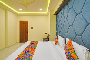 A hotel room with a bed, a ceiling fan, a door, and a wall with a textured design. - Fabhotel Asian International (Hyderabad)