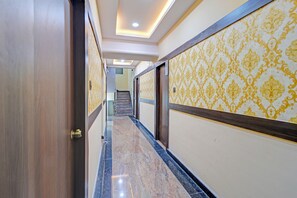 A hallway with marble flooring, patterned wallpaper, and a staircase in the background. - Fabhotel Asian International (Hyderabad)