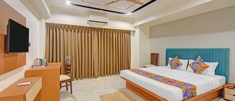 Habitación de hotel con cama, escritorio, silla, televisor y ventilador de techo.