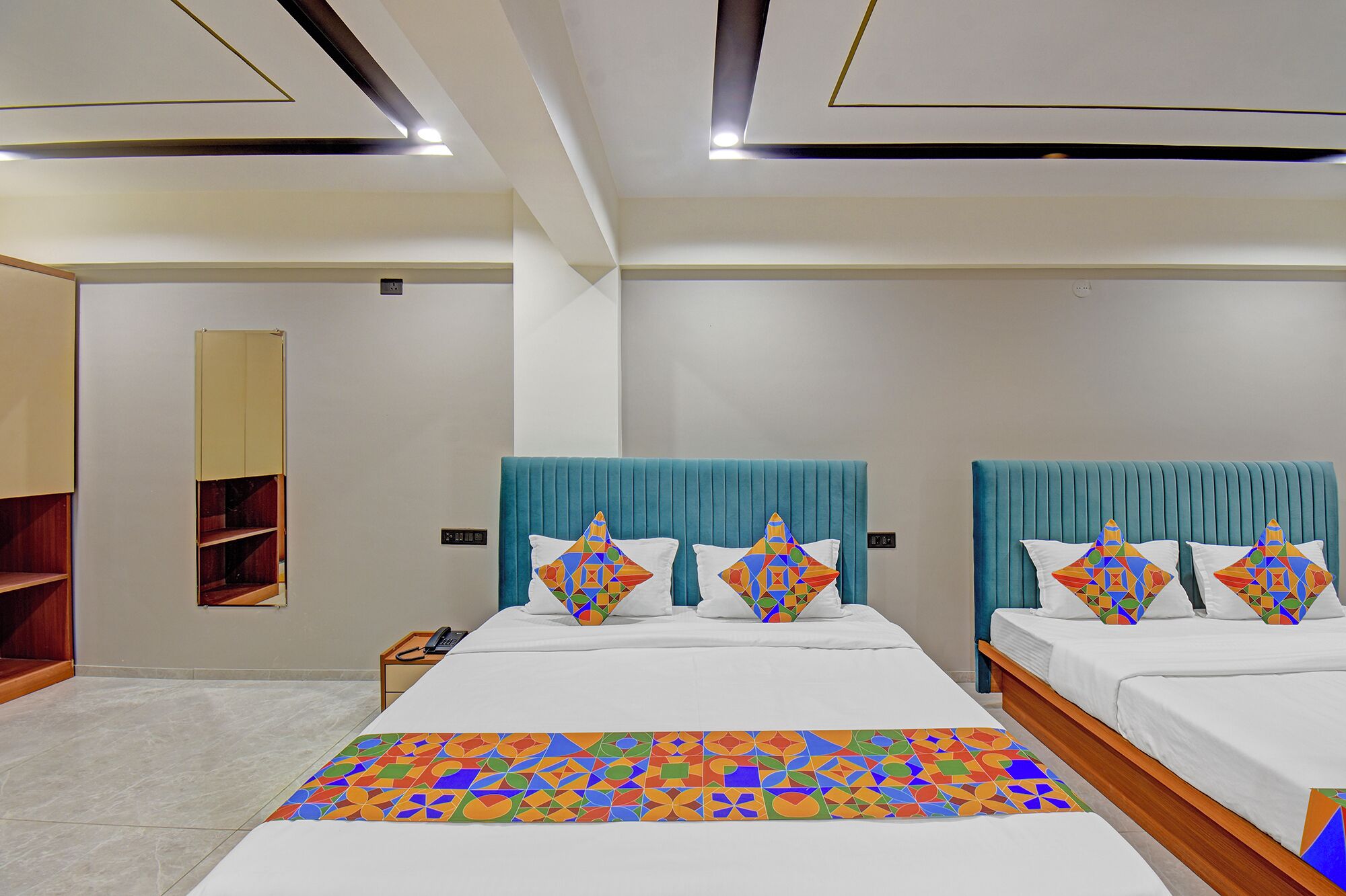 A hotel room with two beds, a large mirror, and a wooden shelf unit.