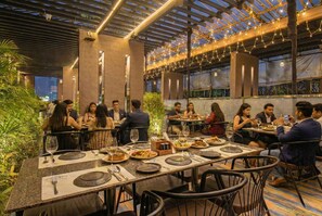 A restaurant with outdoor seating, tables set with plates, glasses, and cutlery, and guests dining. - Fabhotel New Moshi Grrand (Pune)