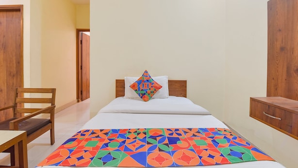 Een hotelkamer met een bed, een houten stoel, een houten kledingkast en een kleurrijke deken met een geometrisch patroon.