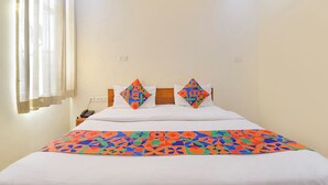 Een hotelkamer met een bed, twee kussens met geometrische patronen, een nachtkastje met telefoon en een raam met gordijnen.
