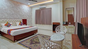 A hotel room with a bed, a desk, a chair, a TV, a ceiling fan, and an air conditioning unit. - FabHotel Lakewood Gardenia Bangalore (Anekal)