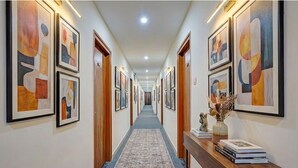 A hallway with framed abstract art on the walls, a patterned carpet, and a wooden console table with books and a vase of dried flowers. - FabHotel Lakewood Gardenia Bangalore (Anekal)