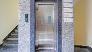 An elevator with a digital display, a marble wall, and several informational signs. - Fabhotel Aashray (Hyderabad)