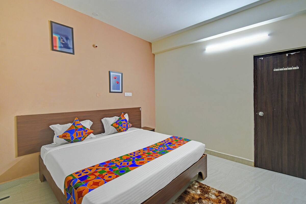 A neatly made bed with a colorful geometric-patterned bedspread, a wooden headboard, and two framed pictures on the wall.