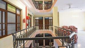 Um saguão de hotel em vários níveis, com uma escadaria central, um extintor de incêndio e uma placa de boas-vindas.