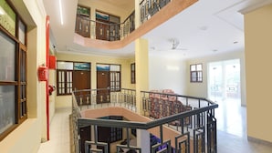 Um interior amplo com uma escadaria central, várias portas com painéis de vidro e um extintor de incêndio vermelho na parede.