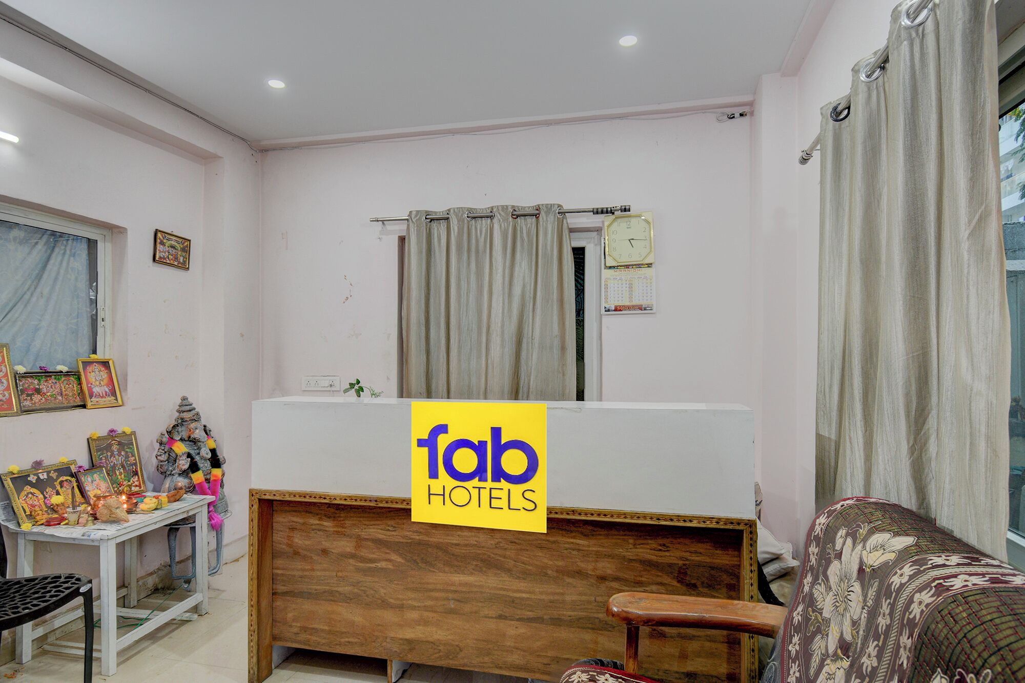 A hotel reception area with a wooden reception desk, a clock, and a calendar on the wall.