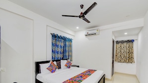 A bedroom with a bed, a ceiling fan, an air conditioning unit, and a window with curtains. - Fabhotel Rk Grand (Hyderabad)
