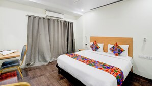 Een hotelkamer met een bed, een bureau, een stoel, een plafondventilator en een raam met gordijnen.