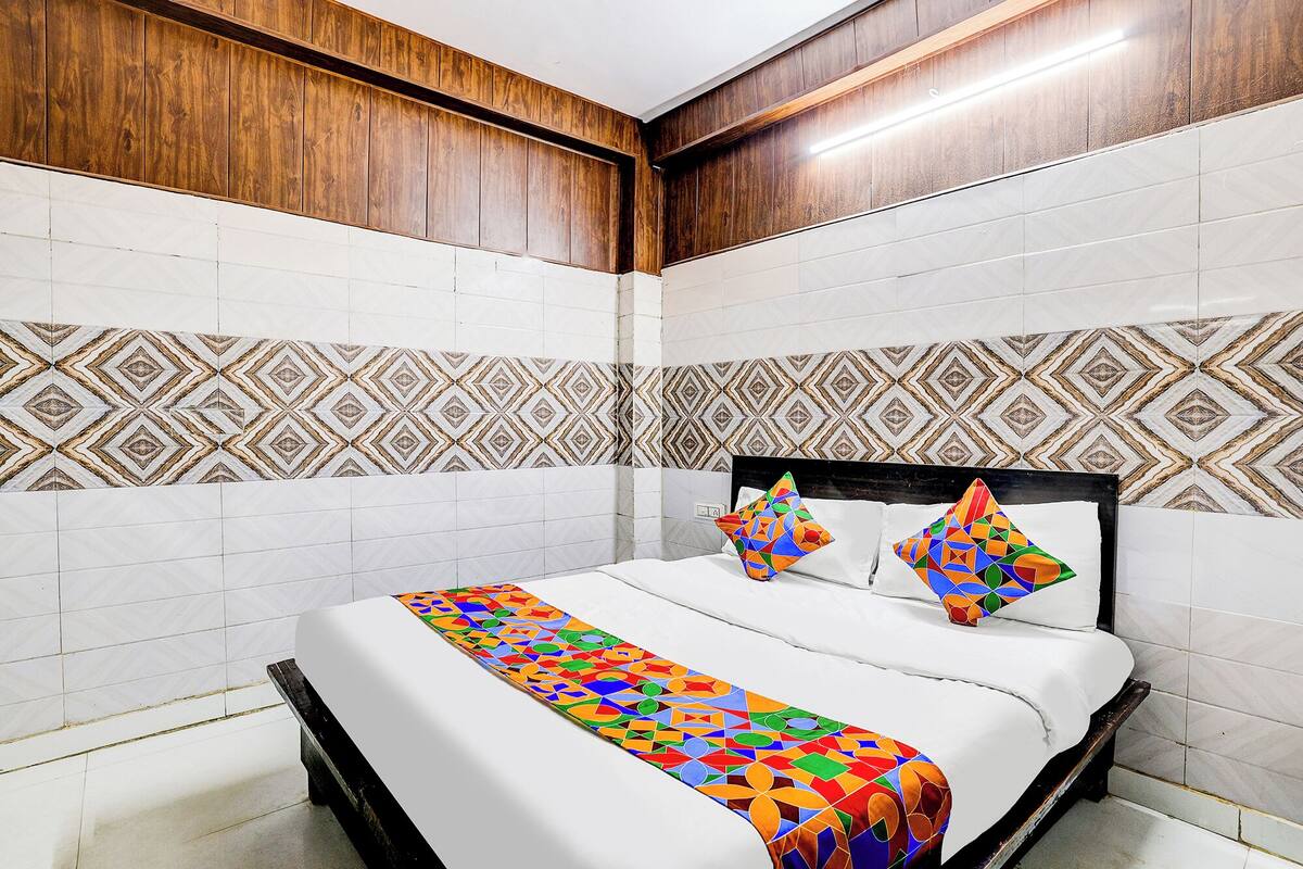 Une chambre d’hôtel avec un lit, des murs recouverts de panneaux de bois, un pare-feu en carreaux décoratifs et une couvre-lit aux couleurs vives.