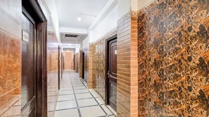 A hallway with marble flooring, a door with a number plate, and a wall with a marbled pattern. - Fabhotel Csrx (Ghaziabad)