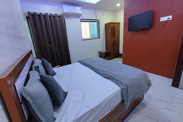 A hotel room with a bed, a TV mounted on the wall, and a window with curtains.