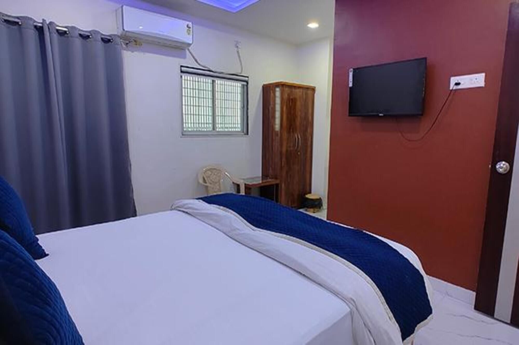Un dormitorio con cama, televisión montada en la pared, ventana con rejas y cortina.