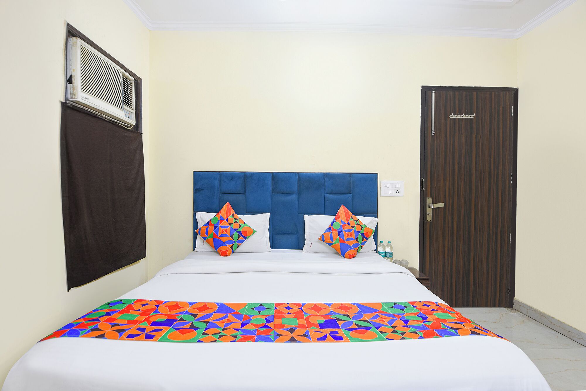 A hotel room with a bed, a headboard, a door, and an air conditioning unit.