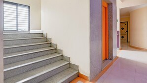 Un escalier avec une fenêtre au-dessus, menant à un couloir où se trouve une porte marquée « SORTIE ».