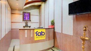 Un espace d’accueil d’hôtel avec un comptoir d’accueil incurvé, une statue religieuse encadrée, un téléviseur fixé au mur et un panneau indiquant le nom de l’hôtel.