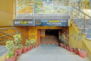 Entrada de un hotel con piso a cuadros, plantas en macetas y un letrero que indica la recepción de Hotel Supreme Suites.
