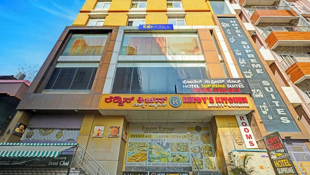Un hôtel à plusieurs étages, avec une enseigne bien visible indiquant « Hotel Supreme Suites » et un restaurant appelé « Reddy’s Kitchen » proposant une cuisine variée.