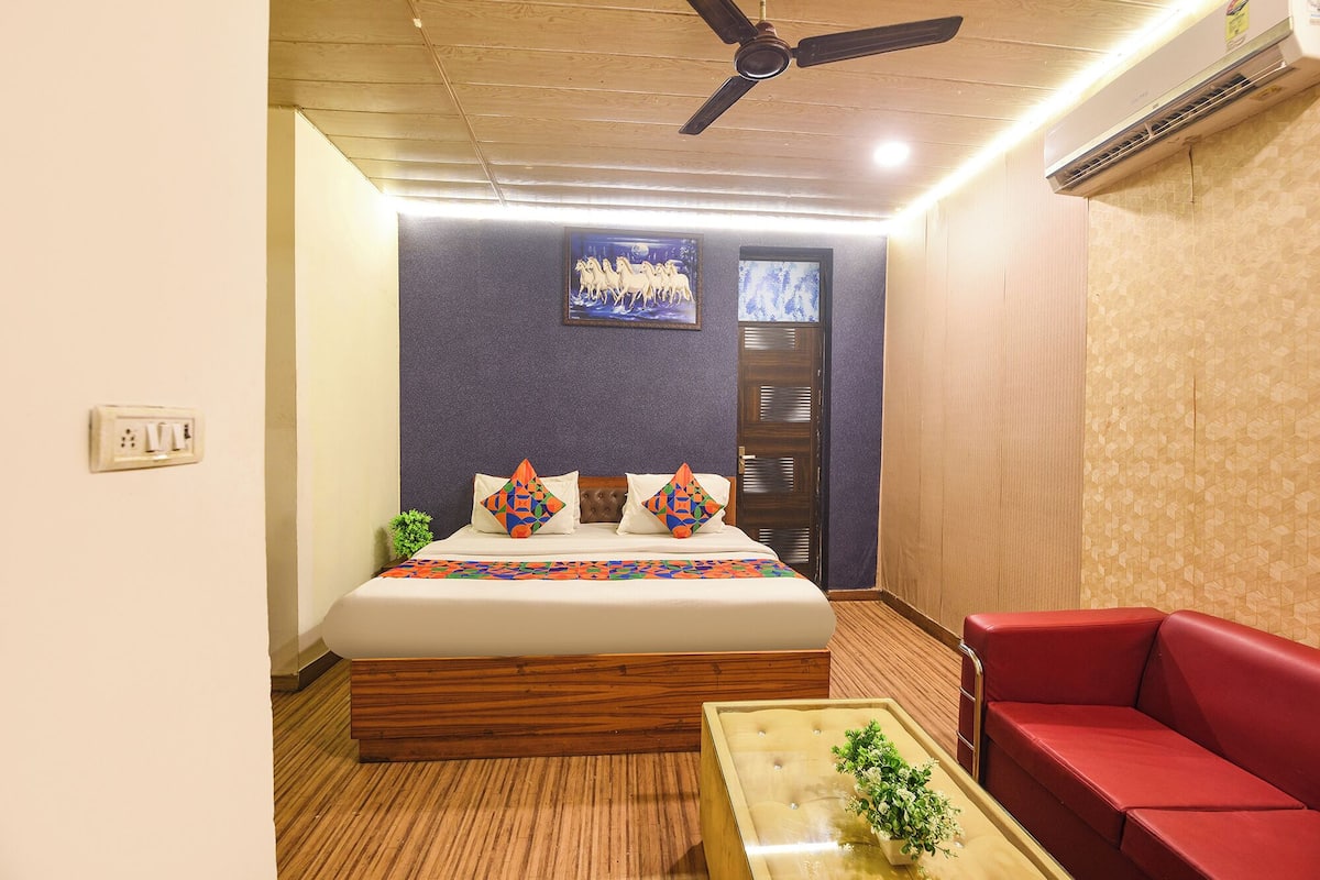 A bedroom with a bed, a red sofa, a small table, and a ceiling fan.
