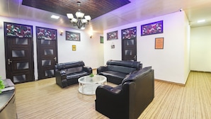 A room with two black leather sofas, a small white table, and a chandelier. There are four doors with camouflage artwork and a sign on one door. - Fabhotel Z Heart (New Delhi)