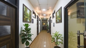 A hallway with wooden flooring, potted plants, framed pictures on the walls, and a door with a number sign. - Fabhotel Z Heart (New Delhi)